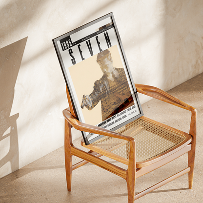 A framed vintage-style poster leaning against a mid-century wooden armchair in a sunlit room. The poster reads '1989 SEVEN' and features a monochrome portrait with a blurred face.