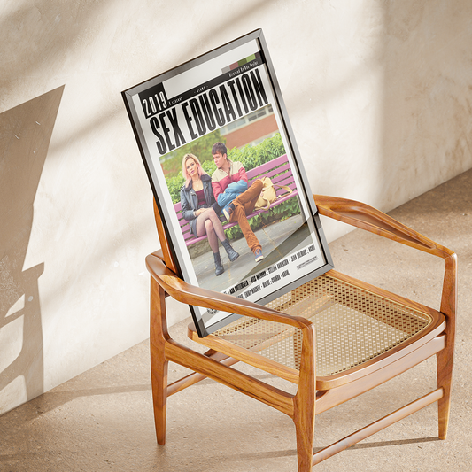 A framed magazine or book cover titled 'SEX EDUCATION' leaning against a wooden armchair in a sunlit room with a textured cream wall.