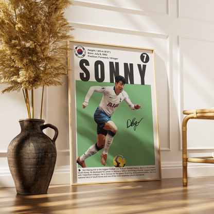 A framed poster featuring a vintage-style football player with the name SONNY and a South Korean crest, leaning against a white paneled wall on a wooden floor beside a vase and chair.