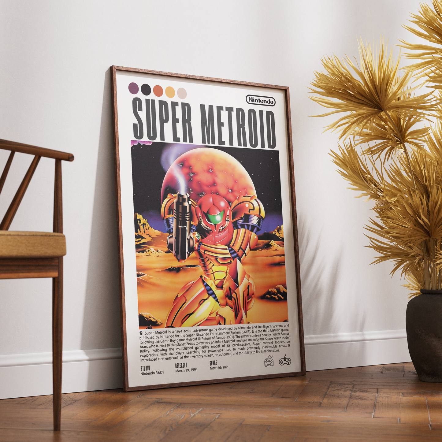 A framed retro-style poster leaning against a white wall on a wooden floor, next to a chair and a potted palm. The poster reads "Super Metroid" and features Samus in gold armor with a red planet in the background.