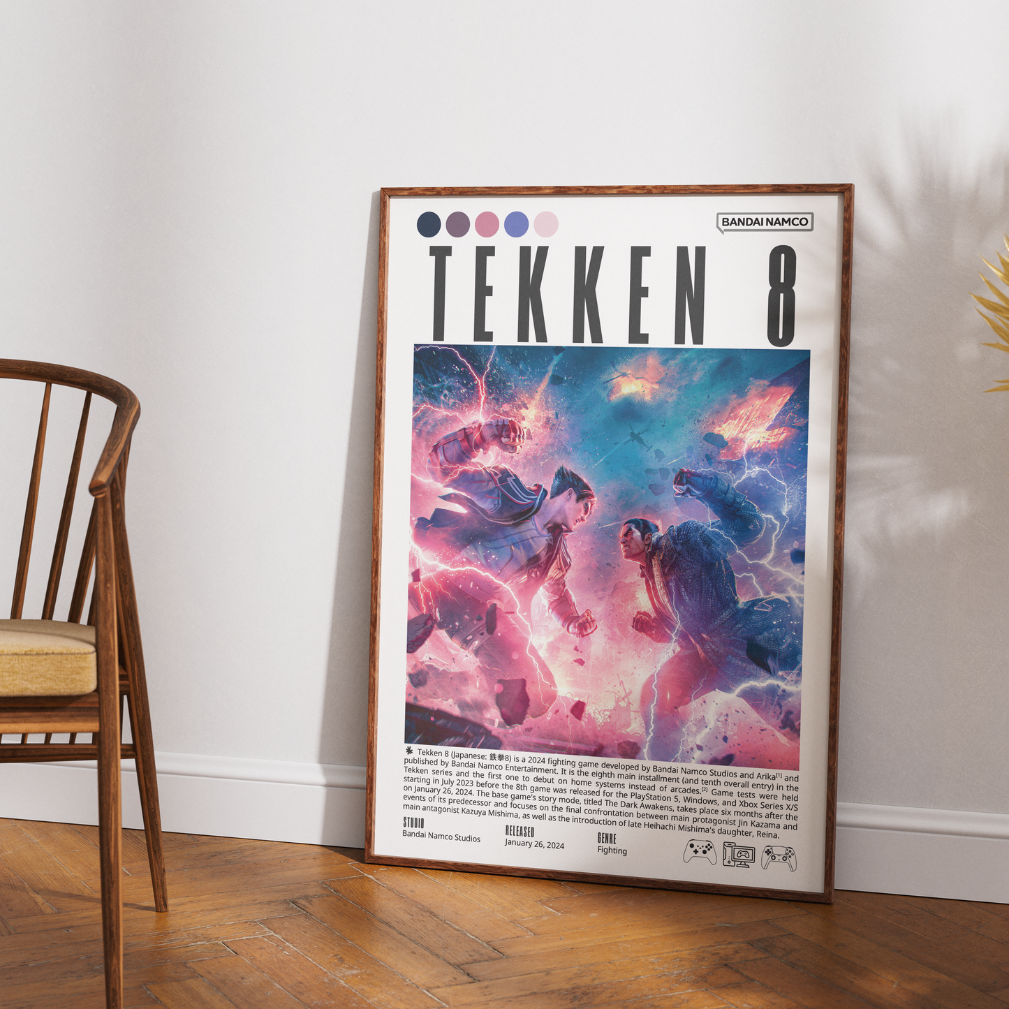 A framed Tekken 8 poster leaning against a white wall on a wooden floor, with part of a wooden chair visible on the left. The poster features colorful anime-style characters and the Tekken 8 title.