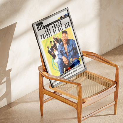 A framed 'The Fresh Prince of Bel-Air' movie poster leaning against a mid-century modern wooden chair with a woven cane seat, set in a sunlit room with textured plaster walls.