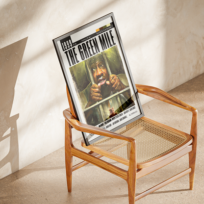 A framed 'The Green Mile' movie poster leaning against a mid-century modern wooden armchair in a sunlit room with textured plaster walls.