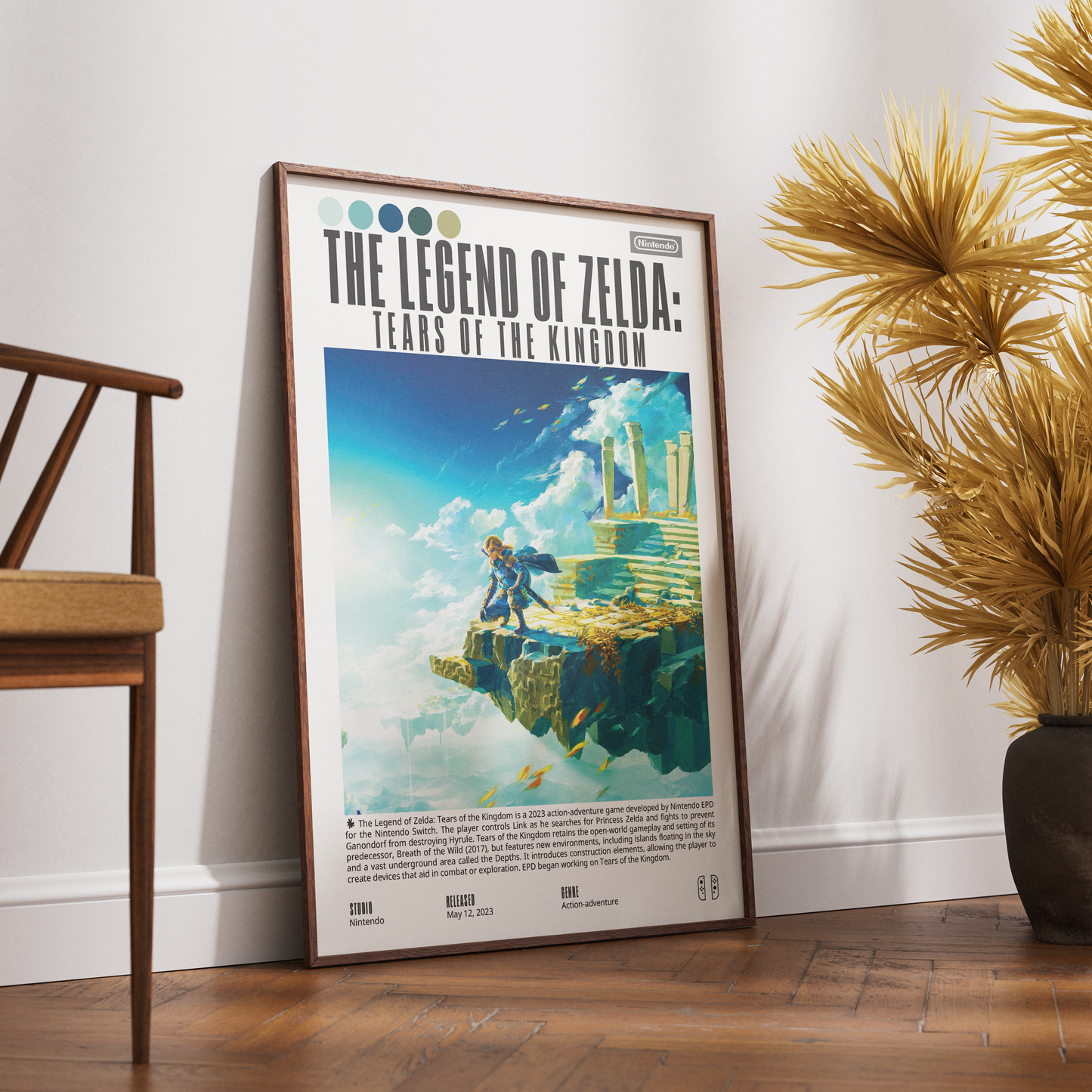 A framed 'The Legend of Zelda: Tears of the Kingdom' poster leaning against a white wall on a wooden floor, with a wooden chair on the left and a potted palm on the right.