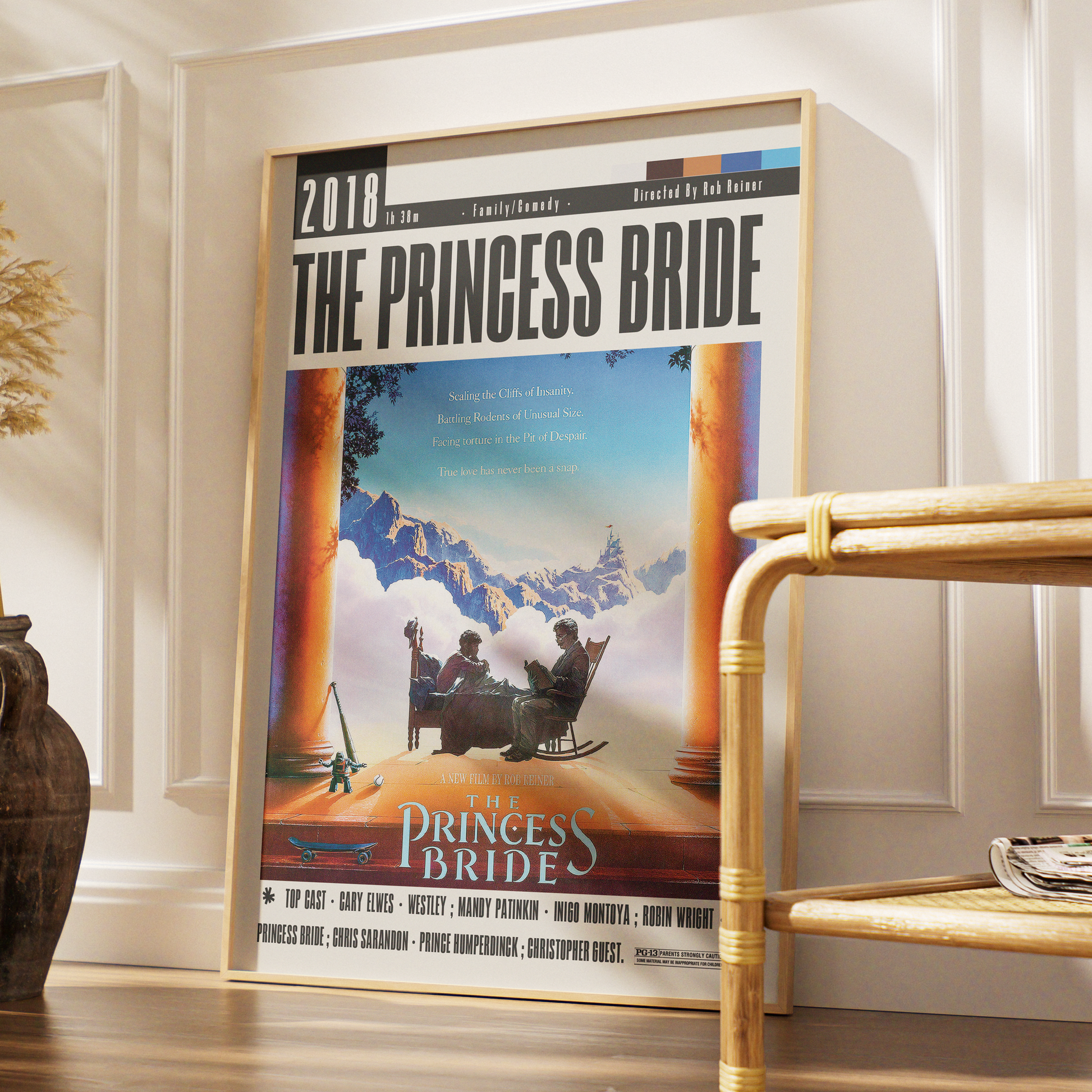 A framed 'The Princess Bride' movie poster leaning against a white paneled wall on a wooden floor, with a bamboo side table and decorative vase nearby.