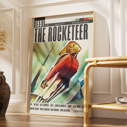 A framed vintage-style poster titled "THE ROCKETEER" leaning against a white paneled wall in a styled interior. The poster shows a red-suited astronaut or space figure with a gold helmet against a green and blue abstract background.