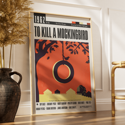 A framed vintage-style poster of the movie 'To Kill a Mockingbird' leaning against a white wall on a wooden floor, styled in a home interior next to a dark ceramic vase with dried grass and a bamboo chair.