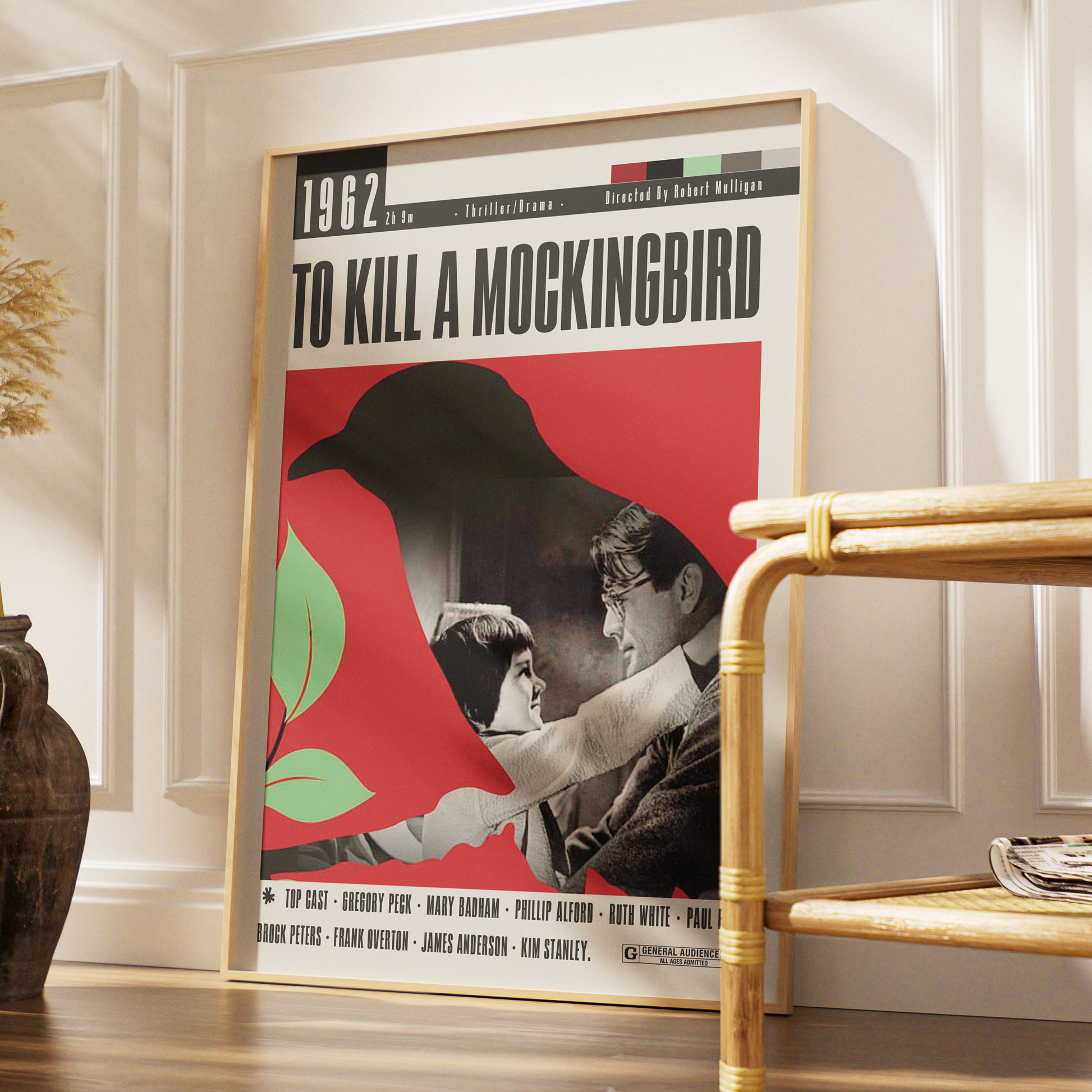 A framed vintage-style movie poster for 'To Kill a Mockingbird' leaning against a white paneled wall in a styled interior. The poster features a large black bird silhouette over a red background, with black-and-white artwork and text.
