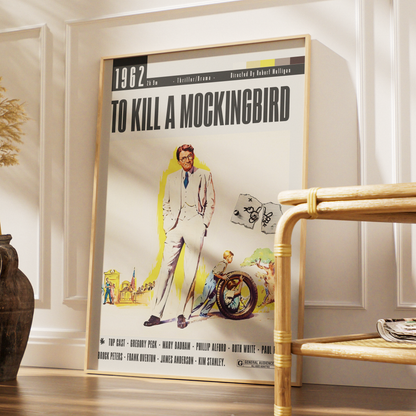 A framed vintage-style movie poster for 'To Kill a Mockingbird' leaning against a white paneled wall in a styled interior. The poster features a cream background with bold black title text, an illustrated man in a light suit, a motorcycle, and small scenic accents.