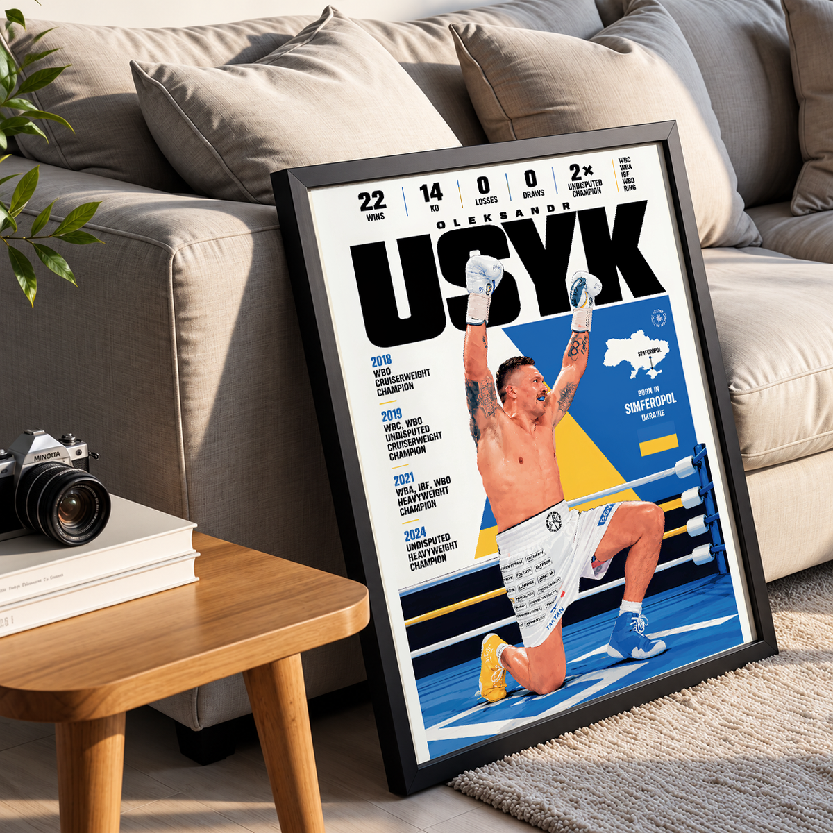A framed poster print leaning against a beige sofa in a living room setting. The poster features a stylized boxing-themed cover with the name 'OLYUK' at the top, a shirtless boxer kneeling in a ring with arms raised, and multiple years listed on the left side.