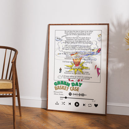 A framed custom music-themed art print leaning against a white wall on a wooden floor next to a wooden chair. The print features a parody of the Green Day 'Basket Case' album cover with a cassette graphic, song lyrics, and album-style controls.