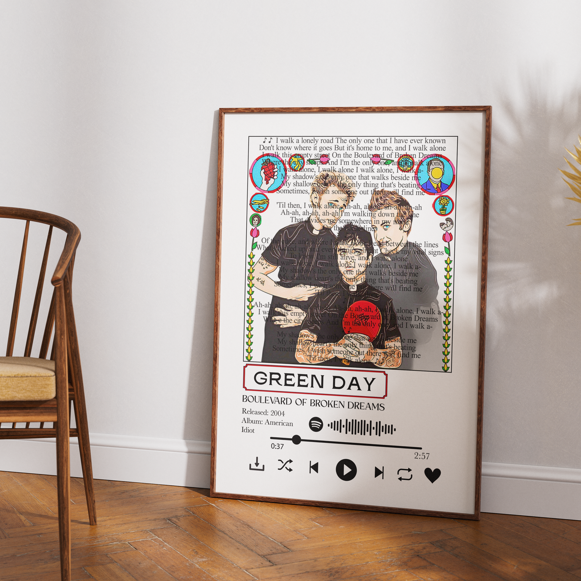 A framed music-themed art print of Green Day's 'Boulevard of Broken Dreams' leaning against a white wall on a wooden floor next to a wooden chair.