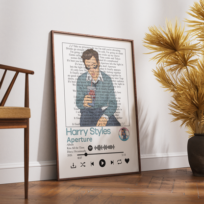 A framed personalized music poster leaning against a white wall on a wooden floor, styled in a room with a chair and a potted plant. The poster features a custom illustration of Harry Potter holding a phone, with song lyrics printed in the background and the title 'Harry Styles Aperture' at the bottom.