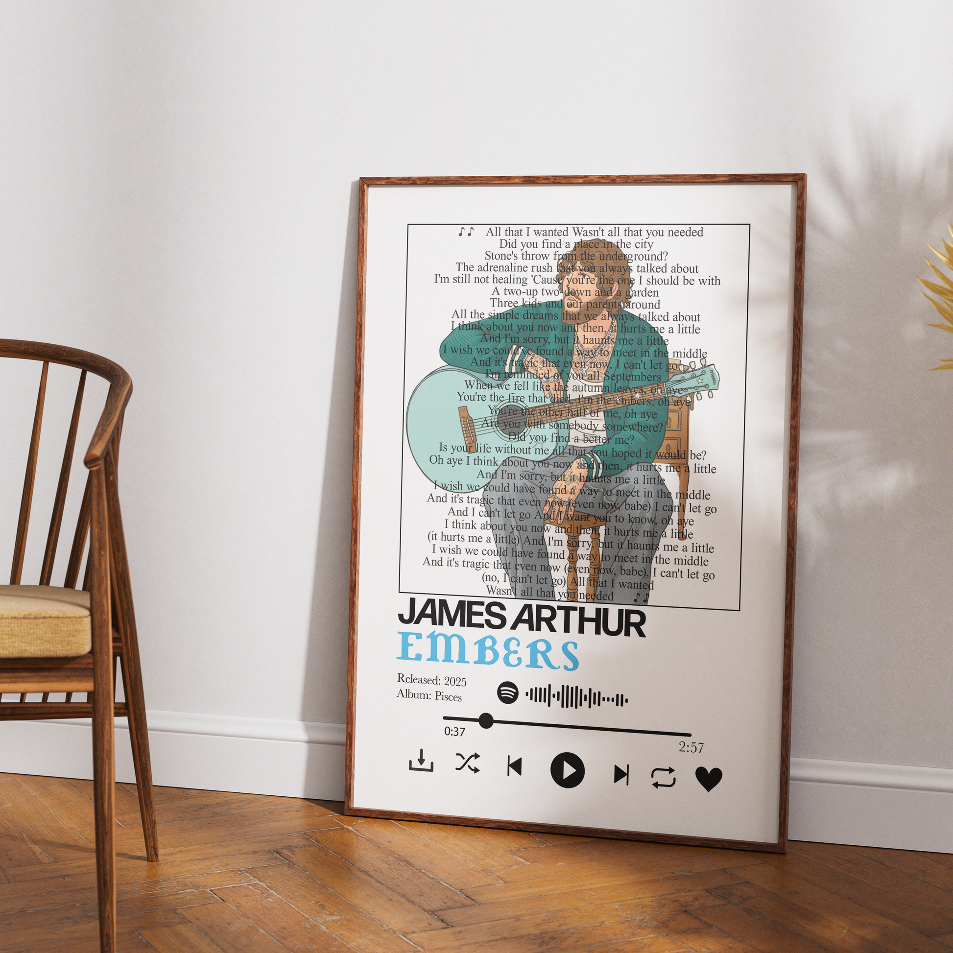 A framed personalized song poster featuring James Arthur Embers, styled leaning against a white wall on a wooden floor next to a wooden chair.