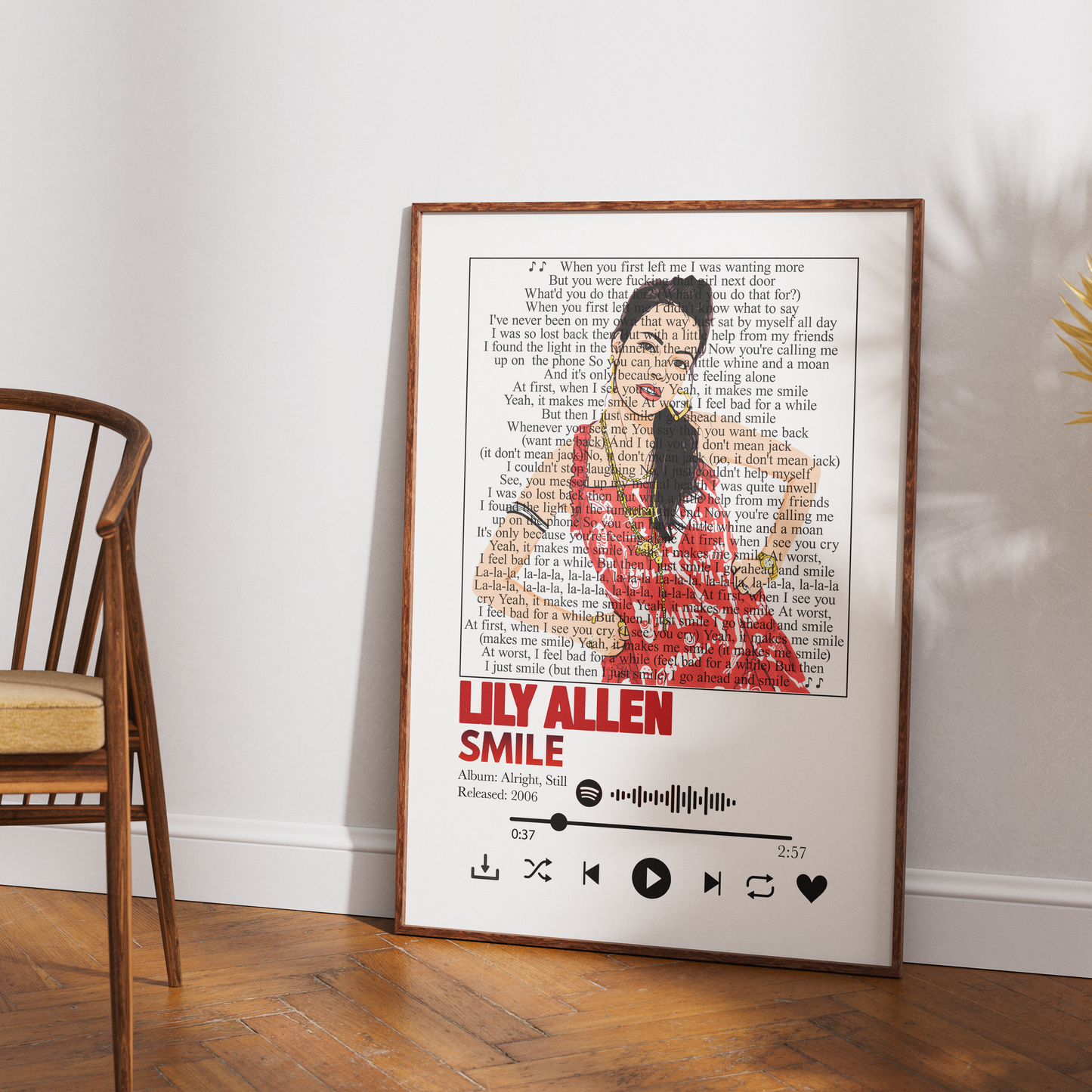 A framed art print featuring a stylized portrait of Lily Allen from The Nightmare Before Christmas, composed of book text and song lyrics, leaning against a white wall on a wooden floor next to a wooden chair.
