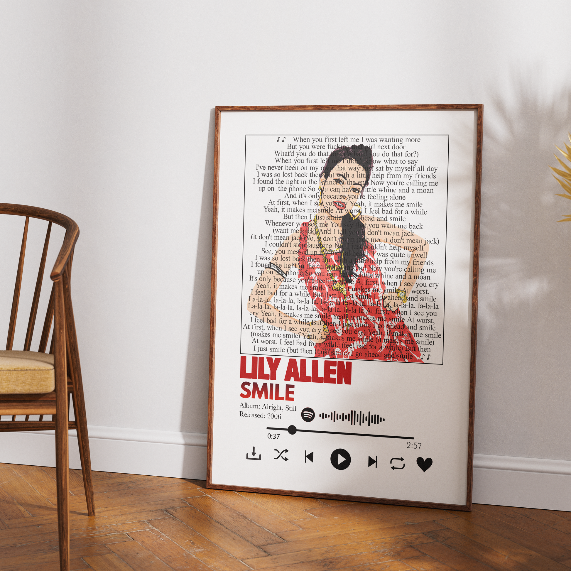 A framed art print featuring a stylized portrait of Lily Allen from The Nightmare Before Christmas, composed of book text and song lyrics, leaning against a white wall on a wooden floor next to a wooden chair.