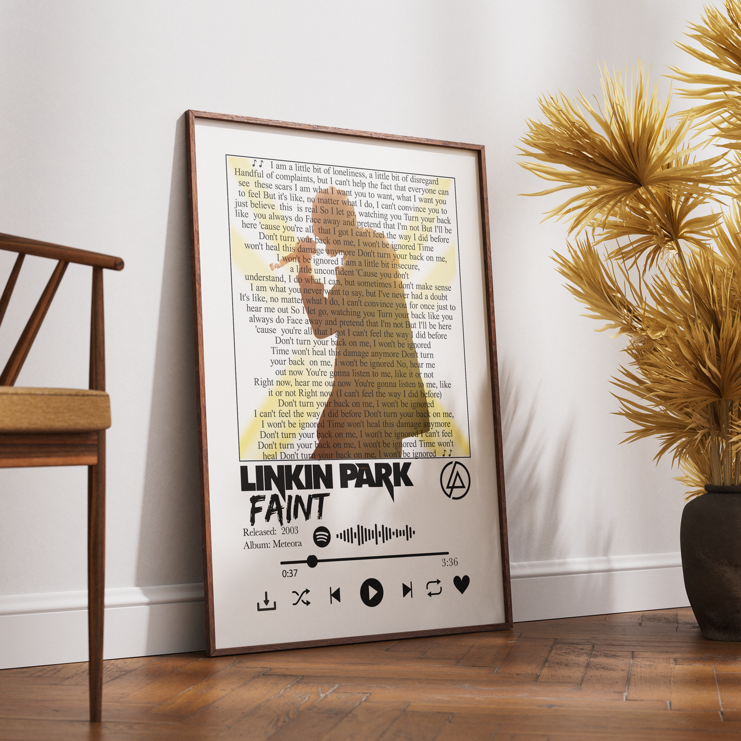 A framed Linkin Park 'Faint' poster leaning against a white wall on a wooden floor, styled in a room with a wooden chair and a potted palm.
