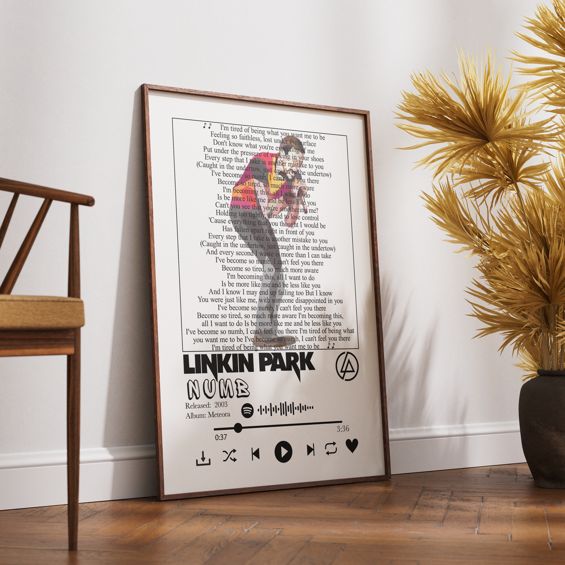 A framed Linkin Park 'Now Here' music poster leaning against a white wall on a wooden floor, styled in a room with a wooden chair and a potted palm.