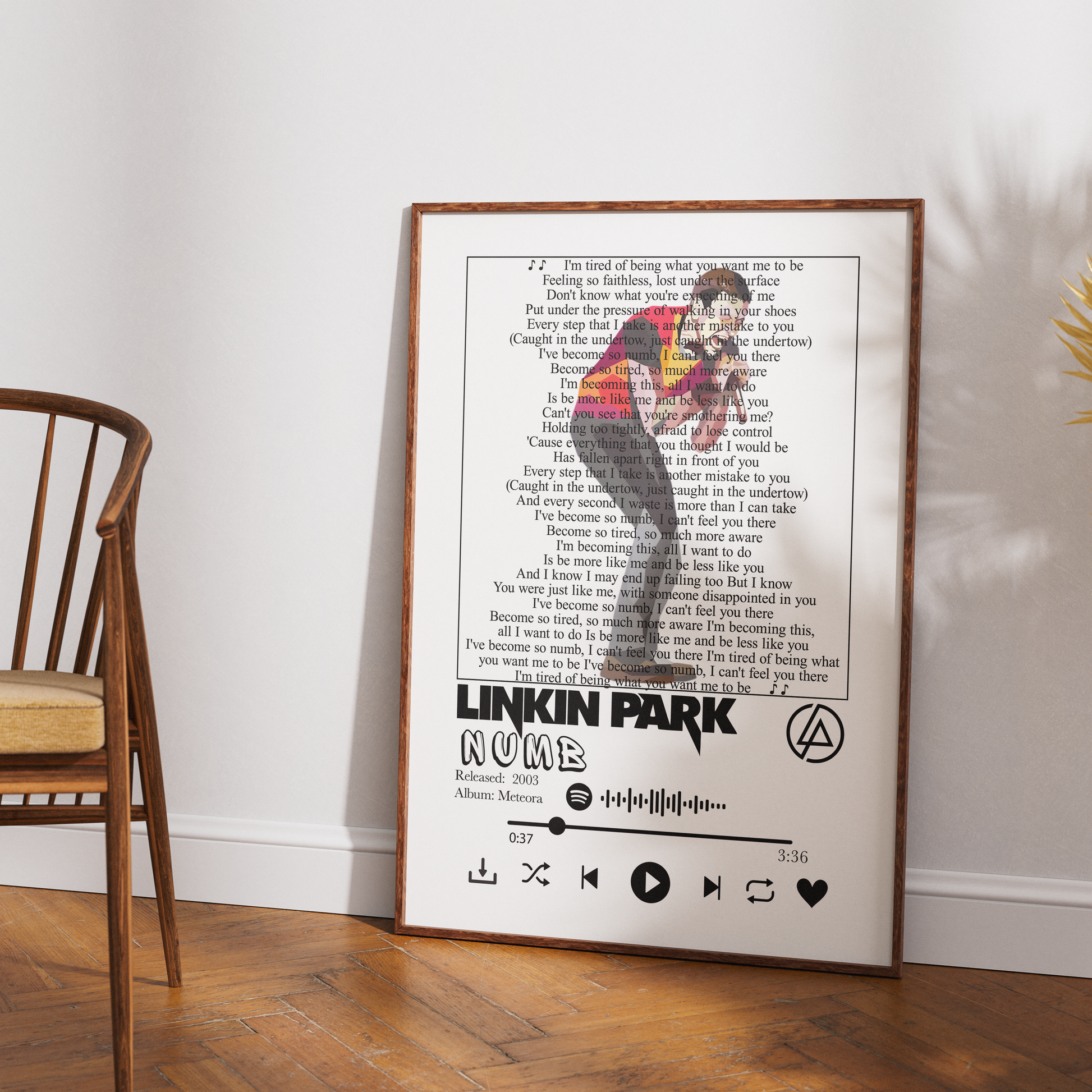 A framed music poster of Linkin Park's album 'Numb' leaning against a white wall on a wooden floor, next to a wooden chair.