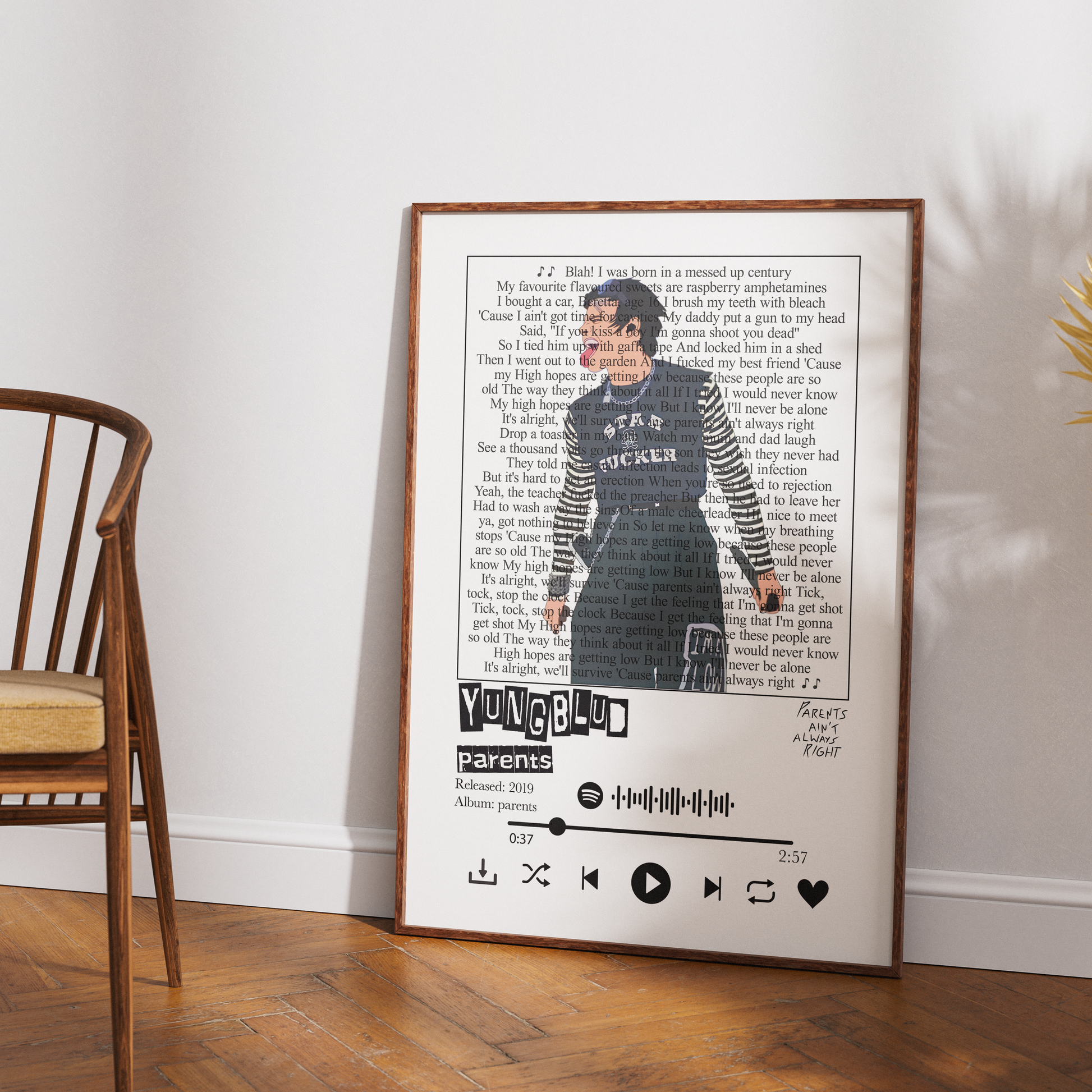 A framed custom music-themed art print leaning against a white wall on a wooden floor, next to a wooden chair. The print features a photo of a woman, song lyrics, the name 'YUNG61', and a custom playlist styled like a Spotify interface.